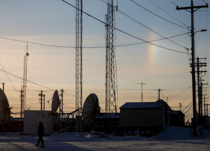 A sundog forms a vertical rainbow as a villager walks by transmission dishes in Kaktovik, Alaska, Tuesday, Oct. 15, 2024. (AP Photo/Lindsey Wasson)