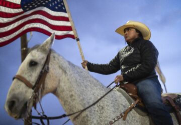 A Navajo horsewoman carries a U.S. flag as she waits for the start of the Western Navajo Fair opening ceremony in Tuba City, Ariz., Friday, Oct. 18, 2024. Native people were first recognized as U.S. citizens 100 years ago, but Arizona prevented them from exercising their right to vote until 1948. (AP Photo/Rodrigo Abd)