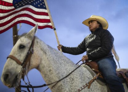 A Navajo horsewoman carries a U.S. flag as she waits for the start of the Western Navajo Fair opening ceremony in Tuba City, Ariz., Friday, Oct. 18, 2024. Native people were first recognized as U.S. citizens 100 years ago, but Arizona prevented them from exercising their right to vote until 1948. (AP Photo/Rodrigo Abd)