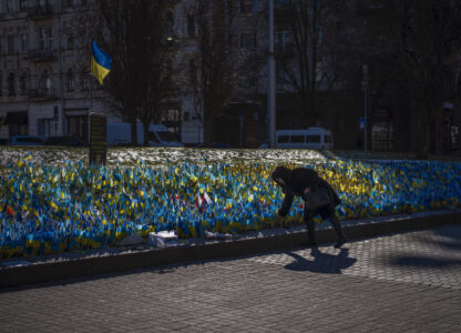 A woman places a Ukrainian flag at a memorial for those killed during the war in Independence Square in Kyiv, Ukraine, Sunday, Feb. 12, 2023. (AP Photo/Emilio Morenatti)