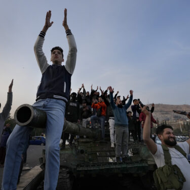 Syrian citizens stand on a government forces tank, that was left on a street, as they are celebrating during the second day of the take over of the city by the insurgents in Damascus, Syria, Monday, Dec. 9, 2024. (AP Photo/Hussein Malla)