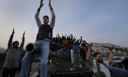 Syrian citizens stand on a government forces tank, that was left on a street, as they are celebrating during the second day of the take over of the city by the insurgents in Damascus, Syria, Monday, Dec. 9, 2024. (AP Photo/Hussein Malla)