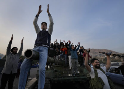 Syrian citizens stand on a government forces tank, that was left on a street, as they are celebrating during the second day of the take over of the city by the insurgents in Damascus, Syria, Monday, Dec. 9, 2024. (AP Photo/Hussein Malla)