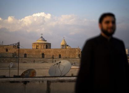 An Armenian Christian deacon walks on a roof terrace near St. James Cathedral, background, at the Armenian quarter in Jerusalem, Thursday, Nov. 21, 2024. (AP Photo/Francisco Seco)