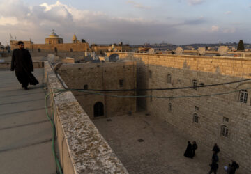 An Armenian Christian deacon walks on a roof terrace near St. James Cathedral, background, at the Armenian quarter in Jerusalem, Thursday, Nov. 21, 2024. (AP Photo/Francisco Seco)