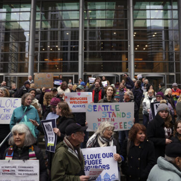 People hold signs as they gather outside the U.S. District Court after a federal judge blocked President Donald Trump's effort to halt the nation's refugee admissions system Tuesday, Feb. 25, 2025, in Seattle. (AP Photo/Ryan Sun)