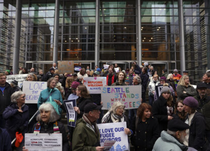 People hold signs as they gather outside the U.S. District Court after a federal judge blocked President Donald Trump's effort to halt the nation's refugee admissions system Tuesday, Feb. 25, 2025, in Seattle. (AP Photo/Ryan Sun)