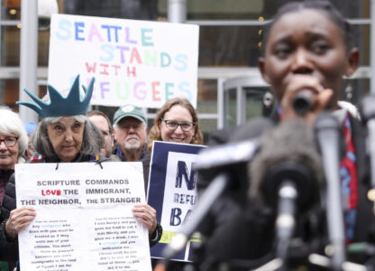 Retired reverend Carrol Jensen wears a hat mimicking the Statue of Liberty as Reverend Emilie Binja, a former refugee from the Democratic Republic of Congo speaks during a rally outside the U.S District Court after a federal judge blocked President Donald Trump's effort to halt the nation's refugee admissions system, Tuesday, Feb. 25, 2025 in Seattle. (AP Photo/Ryan Sun)