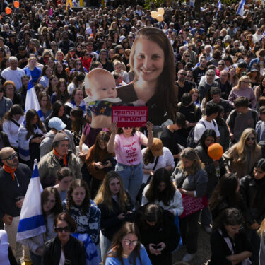 People watch a live broadcast from the funeral of slain hostages Shiri Bibas and her two children, Ariel and Kfir, at a plaza known as the Hostages Square in Tel Aviv, Israel, Wednesday, Feb. 26, 2025. The mother and her two children were abducted by Hamas on Oct. 7, 2023, and their remains were returned from Gaza to Israel last week as part of a ceasefire agreement with Hamas. (AP Photo/Ariel Schalit)