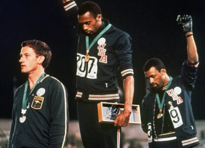 FILE - Extending gloved hands skyward in protest, U.S. athletes Tommie Smith, center, and John Carlos stare downward during the playing of 