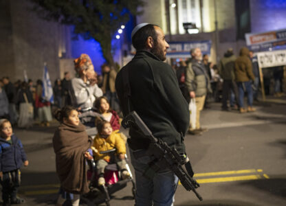 Carrying his weapon a man stands next to his family as he takes part in a protest demanding the continuation of the war against Hamas and the resettlement of the Gaza Strip, in Jerusalem, Thursday, Feb. 27, 2025. (AP Photo/Leo Correa)