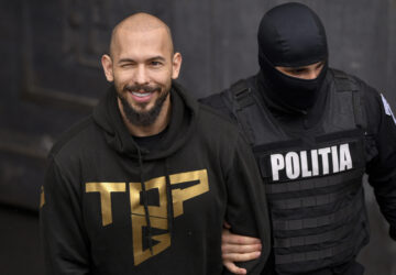 A police officer escorts Andrew Tate, center, handcuffed, from the Court of Appeal in Bucharest, Romania, Tuesday, March 12, 2024. Online influencer Andrew Tate was detained in Romania and handed an arrest warrant issued by British authorities, his spokesperson said Tuesday. (AP Photo/ Alexandru Dobre)