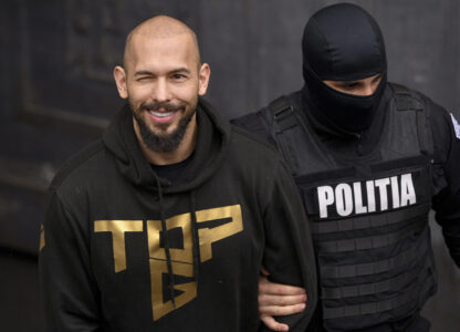 A police officer escorts Andrew Tate, center, handcuffed, from the Court of Appeal in Bucharest, Romania, Tuesday, March 12, 2024. Online influencer Andrew Tate was detained in Romania and handed an arrest warrant issued by British authorities, his spokesperson said Tuesday. (AP Photo/ Alexandru Dobre)