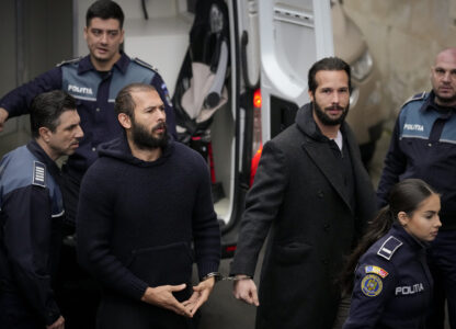 FILE- Police officers escort Andrew Tate, center, handcuffed to his brother Tristan Tate, to the Court of Appeal in Bucharest, Romania, Monday, Feb. 27, 2023. (AP Photo/Andreea Alexandru, File)