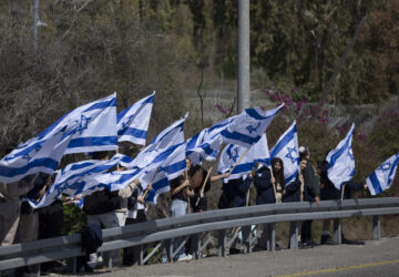 Israelis stand on the side of a road to bid a farewell for the slain hostage Shlomo Mantzur, near the Kibbutz Yad Mordechai, southern Israel, Sunday, March 2, 2025. (AP Photo/Leo Correa)
