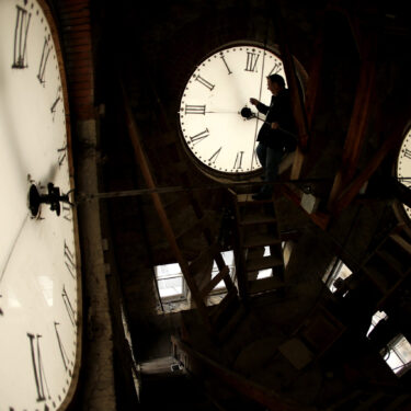 FILE - Custodian Ray Keen inspects a clock face before changing the time on the 100-year-old clock atop the Clay County Courthouse, March 8, 2014, in Clay Center, Kansas. (AP Photo/Charlie Riedel, File)