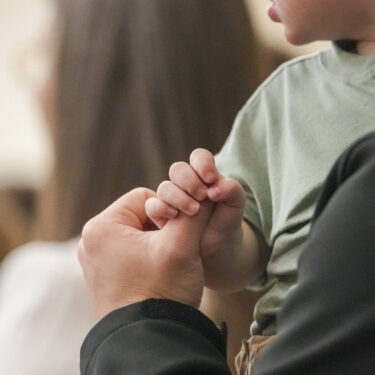 A child holds a man's finger during a service at Community Church of Seminole, Sunday, Feb. 23, 2025, in Seminole, Texas. (AP Photo/Julio Cortez)