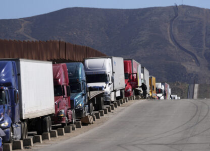 Trucks line up to cross the border into the United States as tariffs against Mexico go into effect, Tuesday, March 4, 2025, in Tijuana, Mexico. (AP Photo/Gregory Bull)