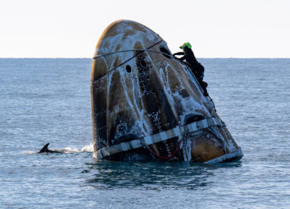 A support team member works on the SpaceX capsule shortly after it landed with NASA astronauts Nick Hague, Suni Williams, Butch Wilmore, and Russia’s Alexander Gorbunov aboard as a dolphin swims past in the water off the coast of Tallahassee, Fla., Tuesday, March 18, 2025. (Keegan Barber/NASA via AP)