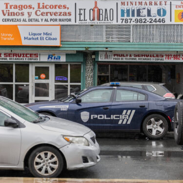 A police car patrols a street in front of a liquor store in Barrio Obrero, San Juan, Puerto Rico, Friday, March 14, 2025. (AP Photo/Alejandro Granadillo)