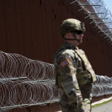 FILE - A member of the military looks on in front of newly-installed concertina wire lining one of two border walls separating Mexico from the United States during a news conference on joint operations involving the military and the Border Patrol, March 21, 2025, in San Diego. (AP Photo/Gregory Bull, File)