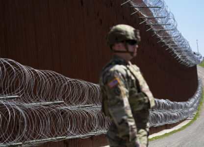 FILE - A member of the military looks on in front of newly-installed concertina wire lining one of two border walls separating Mexico from the United States during a news conference on joint operations involving the military and the Border Patrol, March 21, 2025, in San Diego. (AP Photo/Gregory Bull, File)