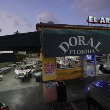 U.S. citizens who immigrated from Venezuela between 16 and 30 years ago play dominos outside El Arepazo, a restaurant that is a hub of the largest Venezuelan community in the U.S., in Doral, Fla., Wednesday, April 2, 2025. Many of the friends, including Cesar Mena, at right, voted for President Donald Trump and continue to support him. 