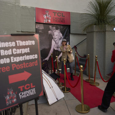 A woman poses for photos on a mock red carpet setup outside TCL Chinese Theatre in Los Angeles, Friday, April 4, 2025. (AP Photo/Jae C. Hong)