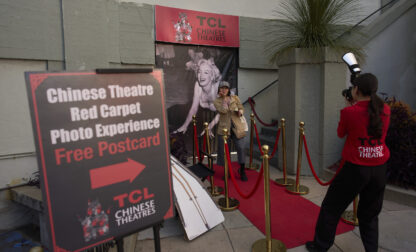 A woman poses for photos on a mock red carpet setup outside TCL Chinese Theatre in Los Angeles, Friday, April 4, 2025. (AP Photo/Jae C. Hong)