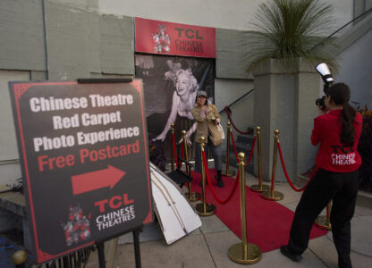 A woman poses for photos on a mock red carpet setup outside TCL Chinese Theatre in Los Angeles, Friday, April 4, 2025. (AP Photo/Jae C. Hong)